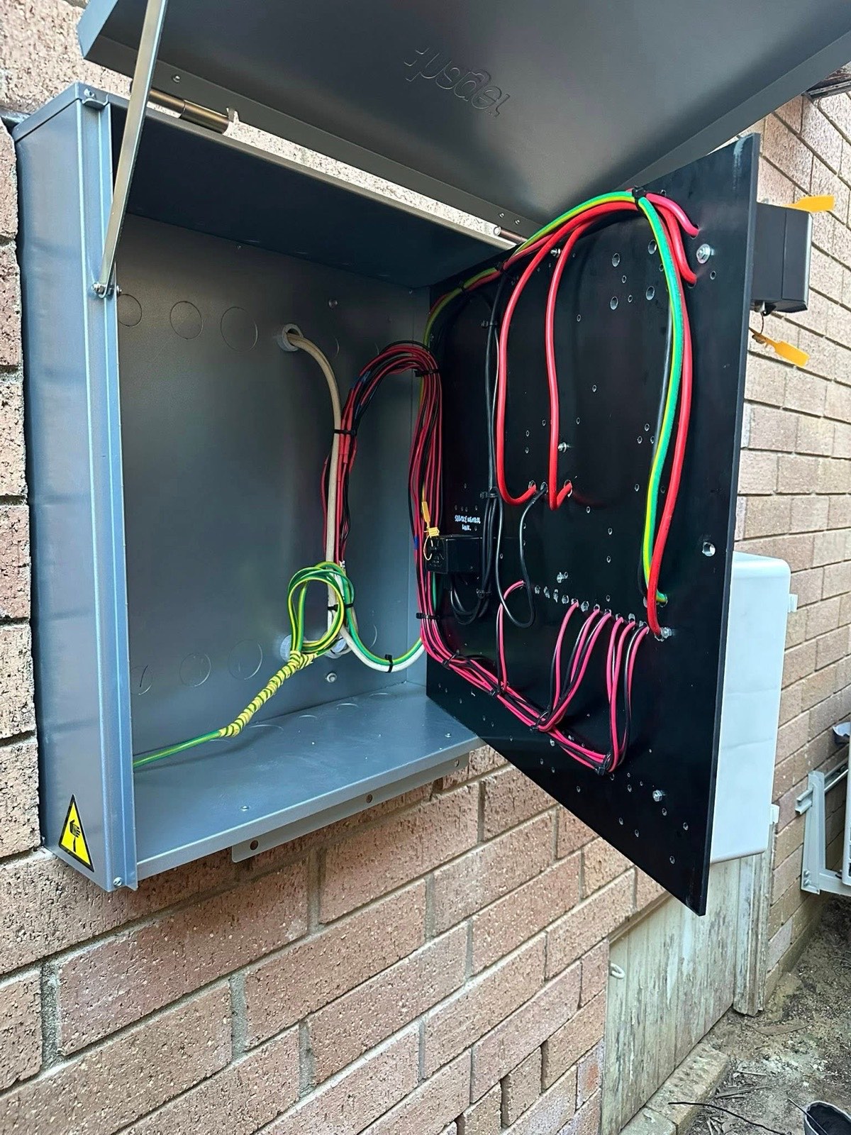 Open meter box with colour-coded wiring on a brick wall