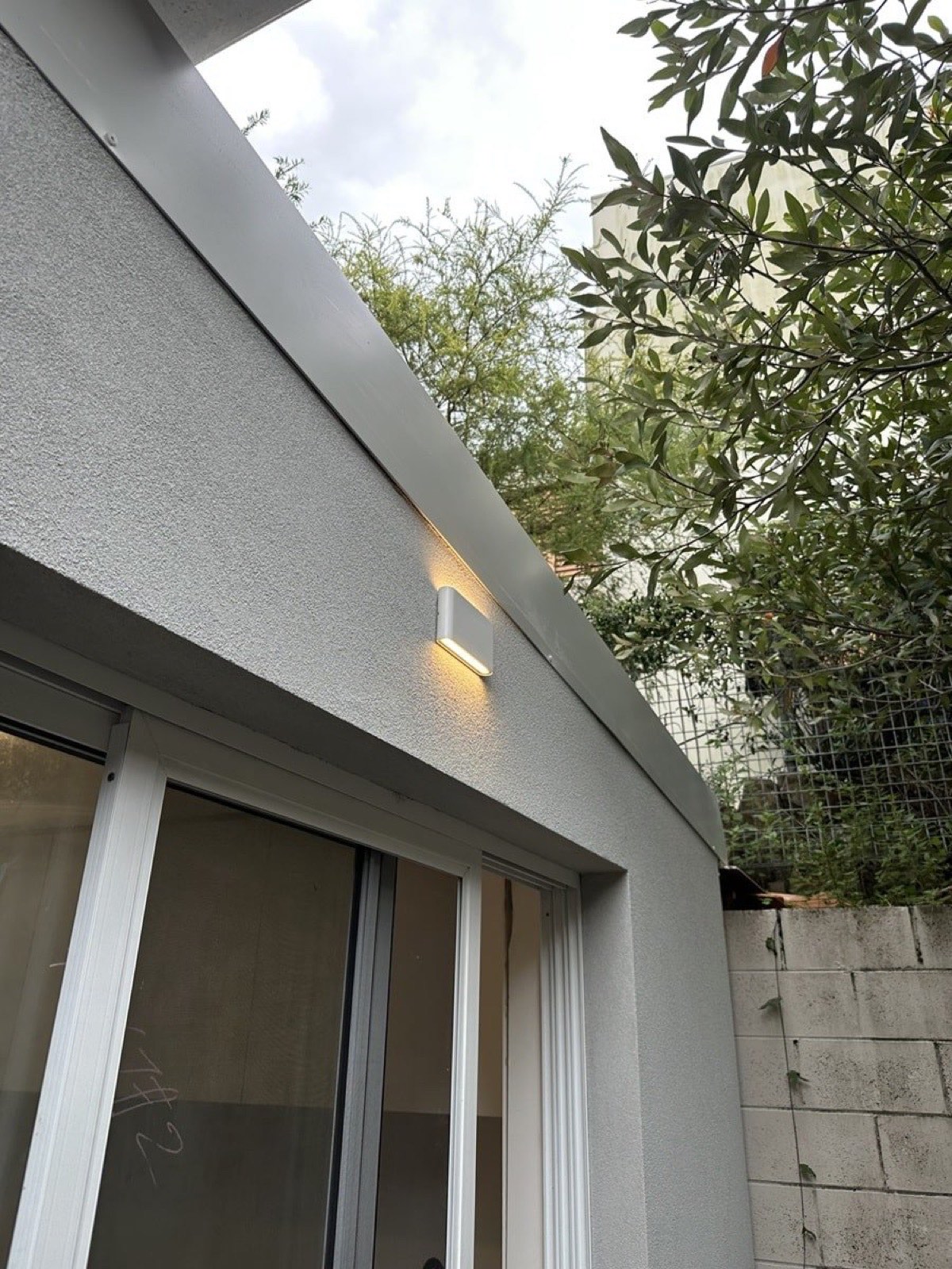 Outdoor wall light installed under the eaves of a rendered home